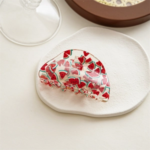 Close-up of a clear acrylic hair claw clip with a red watermelon print on a tray