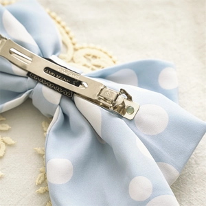 Blue polka dot fabric bow hair clip with silver spring metal fastener and handmade label