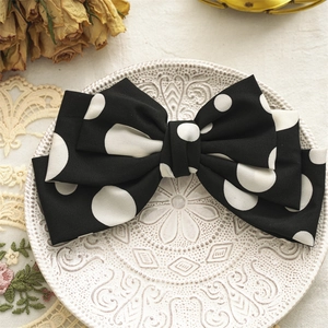 Detailed texture of black polka dot bow hair clip on a vintage white ceramic plate