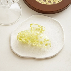 Detailed macro view of yellow acrylic hair claw clip with white floral patterns on stone tray
