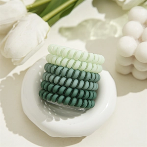 Lot de chouchous spirales mats aux tons verts variés posés sur une table beige