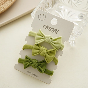 Detailed view of three green bow hair ties on display card with a natural setup