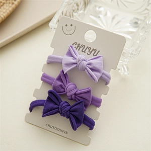 Detailed macro view of three purple bow hair ties on display card with soft lighting