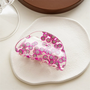 Macro detail of acrylic hair claw clip featuring bright dragon fruit pattern on white surface