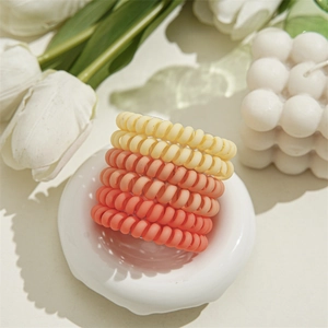 Cinq élastiques à cheveux spirales mats en dégradé de beige et rose sur plateau blanc