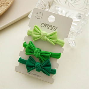 Close-up of three green bow hair ties with vertical rib texture on a display card