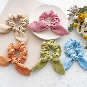 Five pastel rabbit ear scrunchies with pleated texture on a white textured background