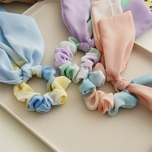 Détails de trois chouchous en mousseline tie-dye avec de longs rubans sur un plateau beige