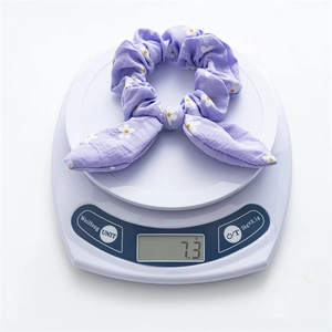 Close-up of a purple daisy print bunny ear scrunchie on a scale weighing 7.3 grams