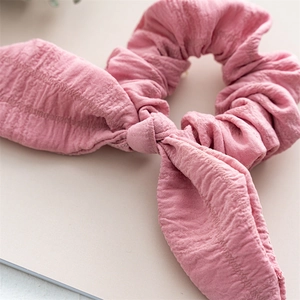 Detail of pink bow scrunchie showing the soft wrinkled fabric texture and elastic band