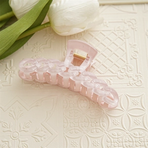 Détail d'une pince à cheveux rose bonbon avec texture chaîne ondulée sur relief beige