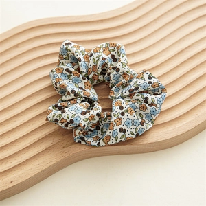 Détail macro d'un chouchou à fleurs bleues et orange sur un plateau en bois