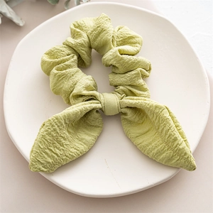 Close-up of light green scrunchie with rabbit ear bow and wavy pleated fabric texture