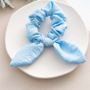 Detailed texture of a light blue rabbit ear scrunchie on a white ceramic display plate