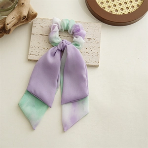 Détail d'un chouchou en mousseline tie-dye violet et vert avec de longs rubans sur pierre