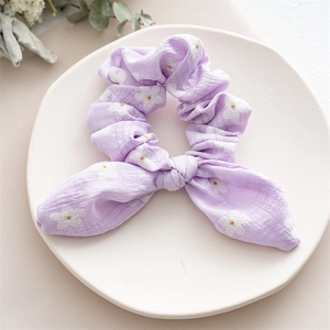 Detailed macro view of purple floral bunny ear scrunchie on a white ceramic tray