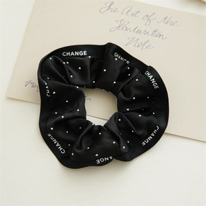Détail du chouchou en satin noir à pois blancs avec logo texte CHANGE élégant