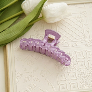 Détail d'une pince à cheveux violette en chaîne avec ressort doré sur socle blanc