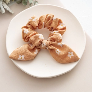 Detail of warm orange scrunchie with daisy print and bow knot on a ceramic tray
