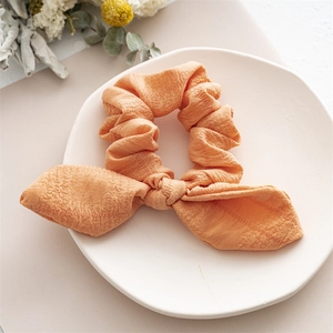 Detailed view of an orange rabbit ear bow scrunchie with crinkled texture on a ceramic plate