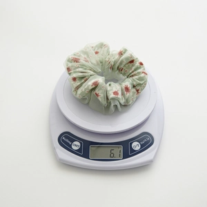 Detail showing the lightweight 6.1g green floral mesh scrunchie on a scale