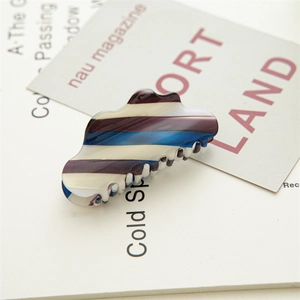 Detail shot of a large striped acetate hair claw clip on a minimalist magazine background