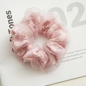 Detail view of double-layered floral mesh scrunchie with pink daisy patterns on a magazine