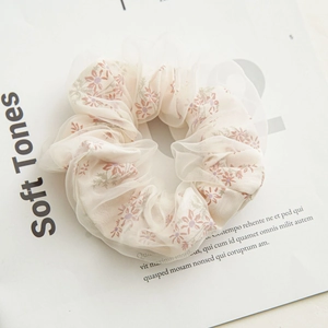 Detail of cream double-layered mesh scrunchie with soft pink floral patterns on fabric