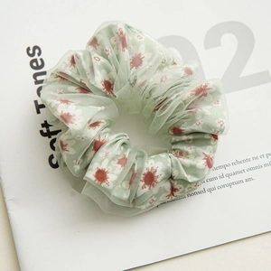 Close-up of light green mesh scrunchie with white daisy prints on a soft paper background