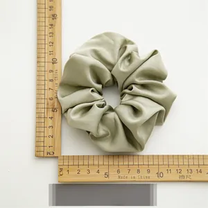 Détail d'un chouchou en satin vert poudré montrant un diamètre de 11 cm sur une règle