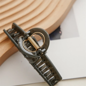 Macro view of olive green resin claw clip with gold metal spring on wooden base
