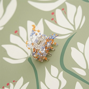 Détail d'une pince à cheveux papillon aux motifs floraux bleus et orange sur base claire