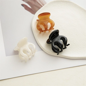 Trois mini pinces à cheveux en résine noir, ambre et blanc crème sur un plateau