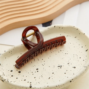 Detailed view of translucent amber hair claw clip with golden spring on ceramic tray