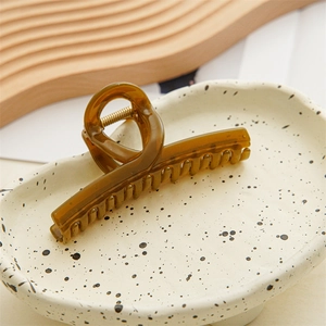 Close-up of amber translucent acrylic hair claw clip with golden spring on ceramic tray