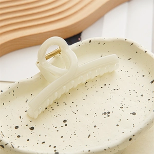 Close-up of a cream-colored matte hair claw clip on a stylish ceramic plate background
