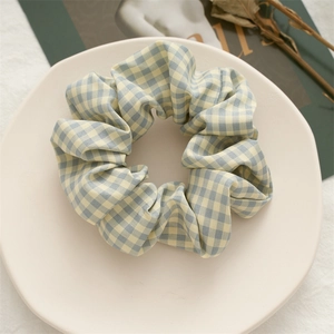 Detail of blue and beige gingham fabric scrunchie on white plate with artistic props