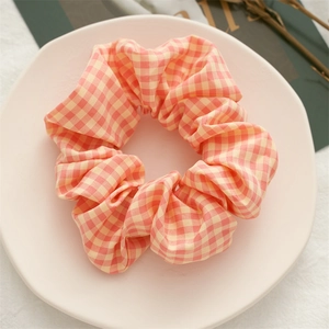 Detail showing the orange plaid fabric texture and elastic structure of the scrunchie