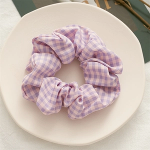 Detailed close-up of a purple gingham checkered hair scrunchie on a ceramic tray