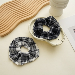 Detail of two pleated plaid scrunchies in black and white checkers on a ceramic plate