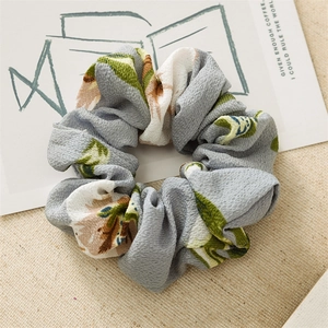 Detail shot of floral print scrunchie with pink flowers on a light grey fabric background