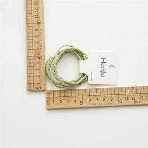 Elastic light green braided hair bands on white card with measurement rulers