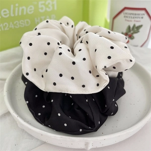 Set di due elastici per capelli in raso a pois neri e bianchi su un piatto di ceramica