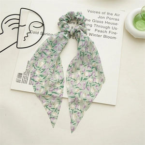 Détail d'un chouchou en mousseline fleurie vert clair avec de longs rubans sur fond blanc