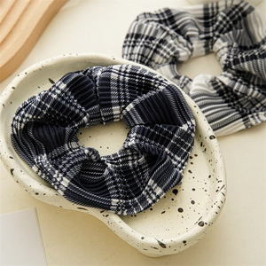 Close-up of pleated checkered scrunchies in navy and monochrome on a ceramic tray