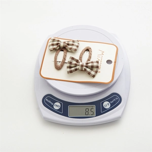 Detailed close-up of plaid bow hair clips showing 8.5g weight on a digital scale