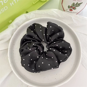 Dettaglio dell'elastico in raso nero a pois bianchi su un piatto in ceramica bianca