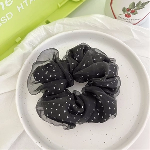 Primo piano di un grande elastico scrunchie in organza nero a pois bianchi su un piatto