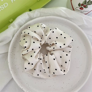 Dettaglio di elastico per capelli in raso con pois neri su tessuto bianco crema