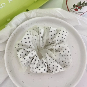 Vista dettagliata di un elastico per capelli in raso bianco a pois neri su piatto decorativo